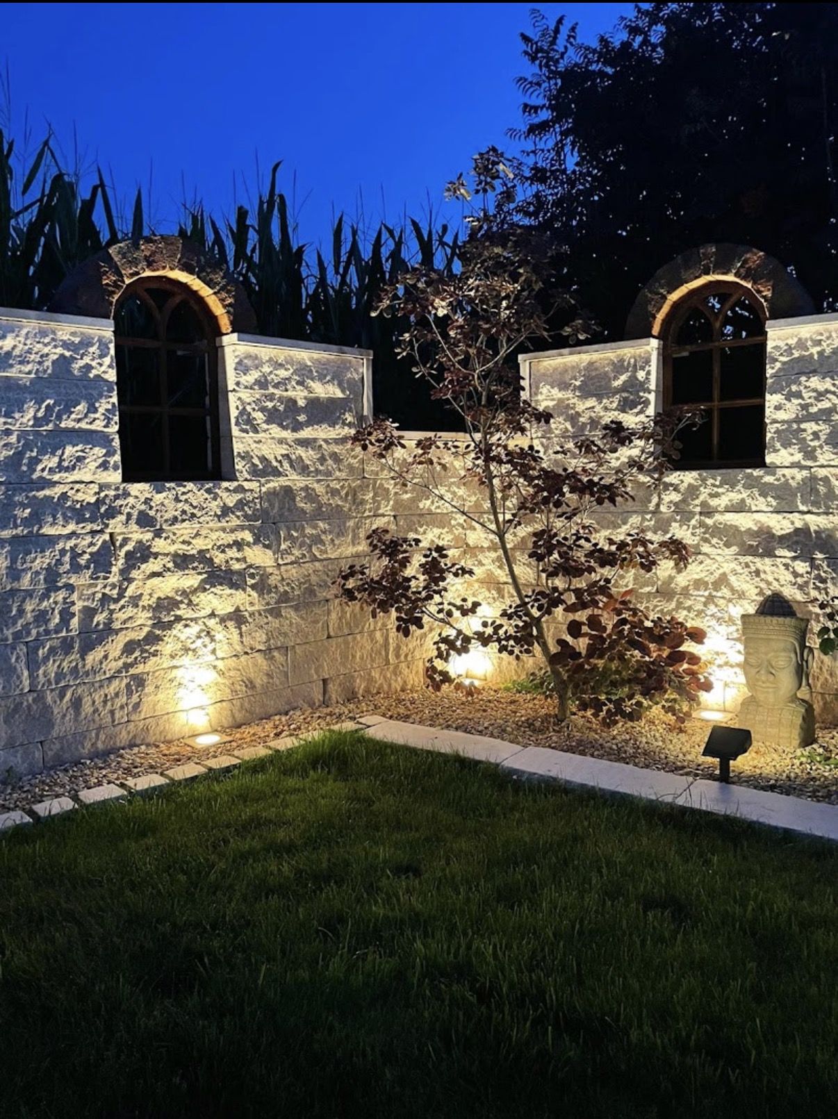 Weiße Natursteinmauer mit Bogenfenstern bei Nacht beleuchtet